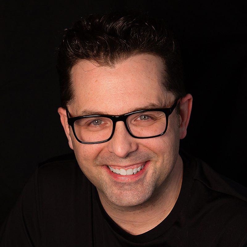 Jason Smith, owner of Rewind VHS Transfers, smiling in a black shirt and glasses
